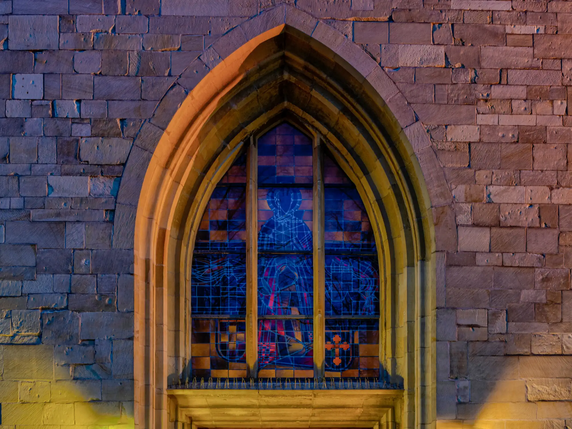 A photograph of a stained-glass window embedded into a deeply recessed archway.